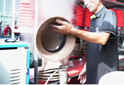 Worker steaming felt hat to shape in factory environment