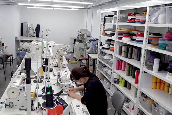 Worker sewing with shelves of colorful threads in workshop.