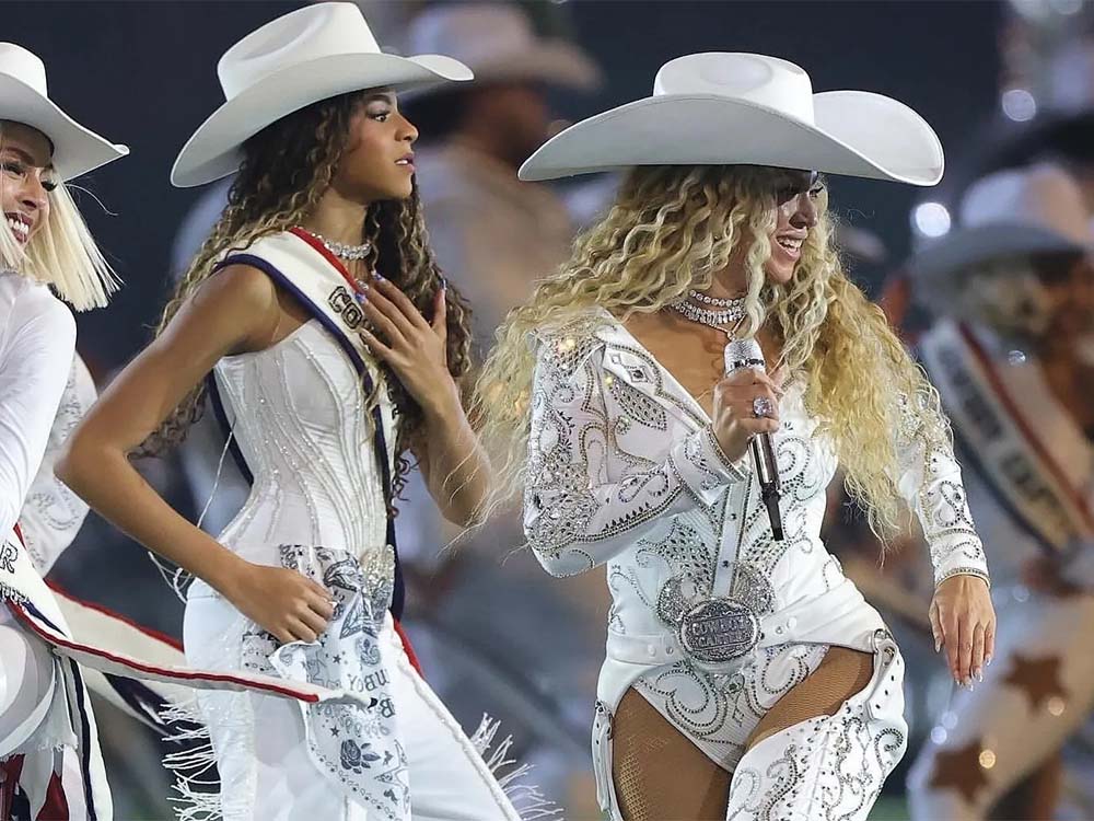 Performers wearing white cowboy hats and decorated white outfits on stage.