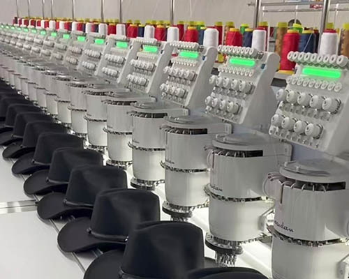 Row of machines embroidering black hats with colorful threads.
