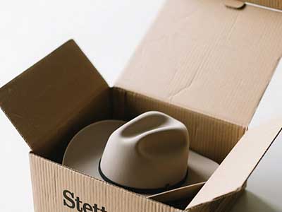 Beige Stetson cowboy hat inside open cardboard shipping box.