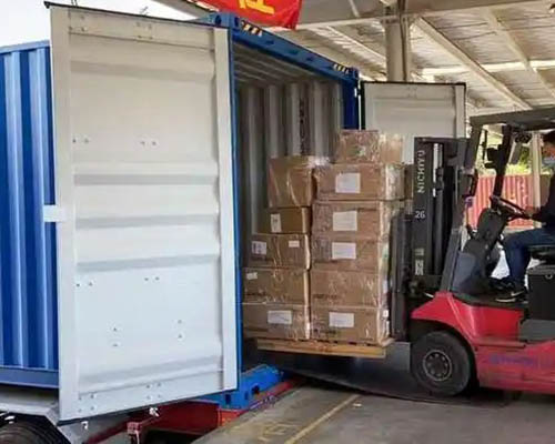 Forklift loading stacked boxes into a blue shipping container.