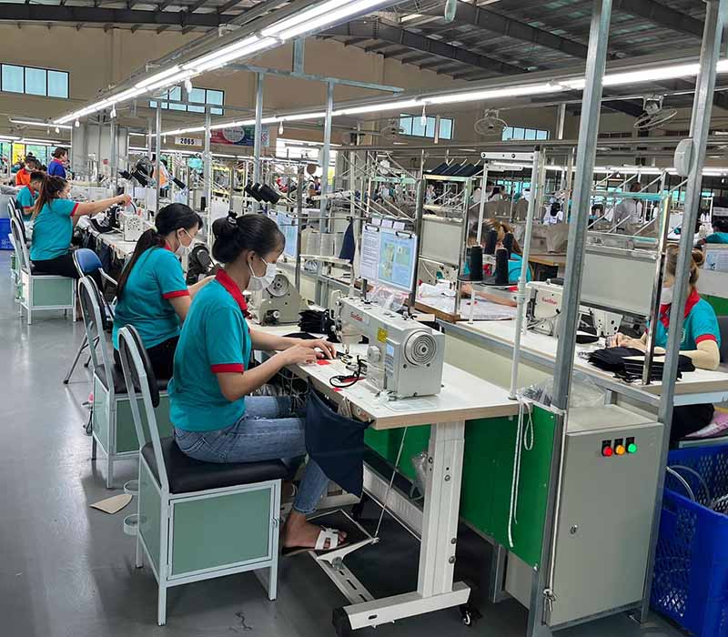 Workers wearing masks sewing fabric at machines in factory.