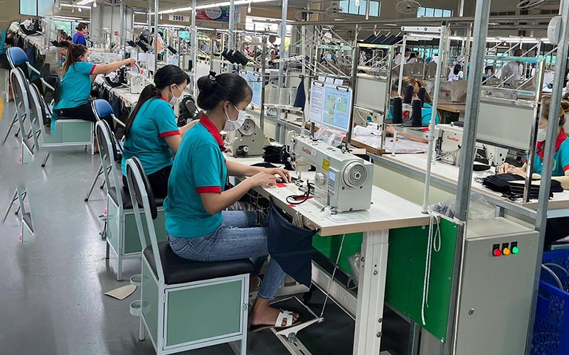 Workers wearing masks sewing clothes on factory production line.