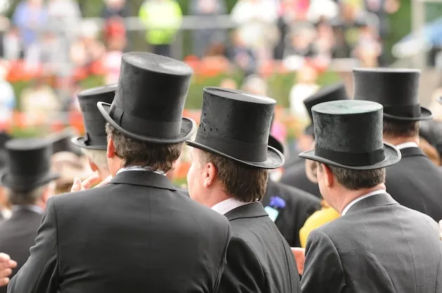 Group of men in black suits wearing traditional black top hats outdoors.
