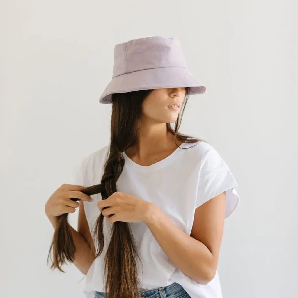 Woman with long braid wearing light purple bucket hat and white t-shirt.