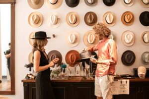 Two people choosing hats in a boutique with hats displayed on the wall