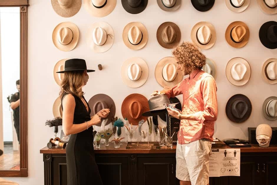 Two people choosing hats in a boutique with hats displayed on the wall