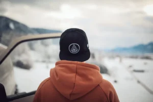 Person in brown hoodie wearing black flat brim snapback cap outdoors