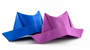 Two folded paper hats in blue and purple on white background
