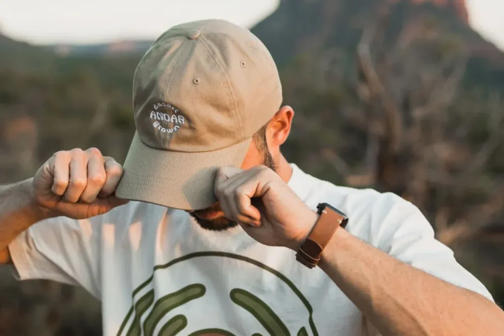 Man outdoors adjusting beige cap with "desert grown" embroidery.