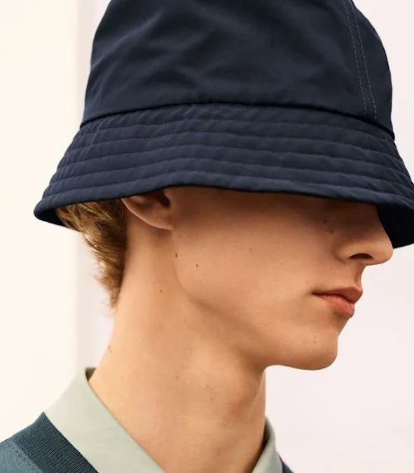 Side profile of man wearing dark blue bucket hat with short hair.