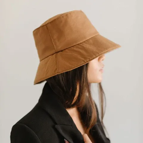 Side view of woman with straight hair wearing brown bucket hat and black jacket.