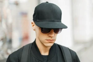 Man wearing black flat brim baseball cap with sunglasses and backpack