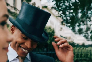 Smiling man wearing elegant black top hat outdoors in formal attire.