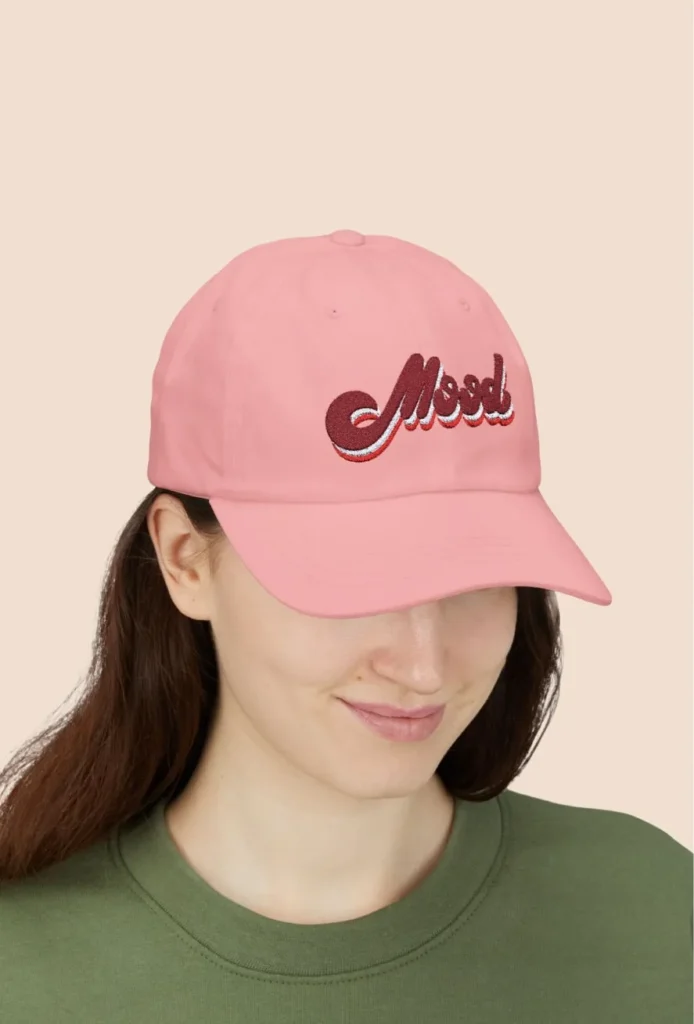 Woman wearing pink cap with "Mood" embroidery, smiling down.